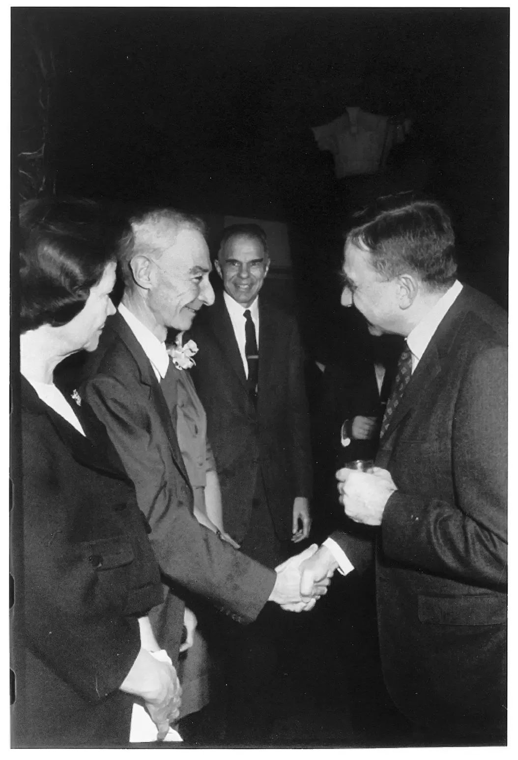 1963年，爱德华·泰勒（右）祝贺奥本海默获得费米奖。奥本海默面露微笑与他握手，姬蒂则面无表情地站在丈夫身边。