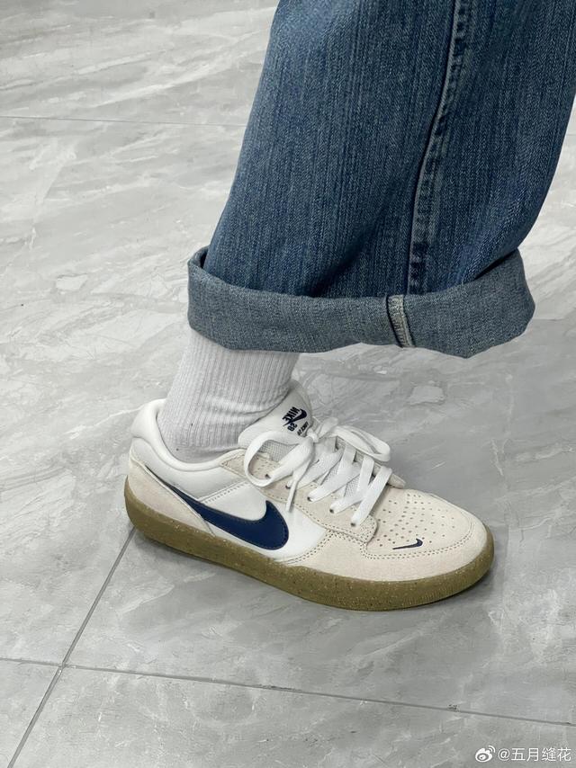 这双Nike SB系列滑板鞋，整体采用米白色麂皮与皮革拼接鞋面，质感柔和且复古。鞋侧标志性Swoosh以藏蓝色皮革呈现，与米白基底形成经典撞色，鞋头处点缀细密透气孔，提升穿着舒适度。白色鞋带搭配同色系