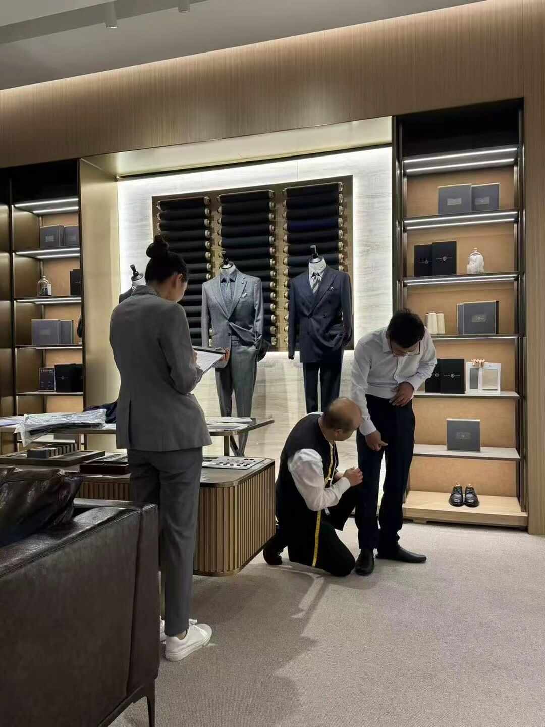 LAMPO定制门店内量体场景，裁缝与顾客在展示台前沟通西装细节