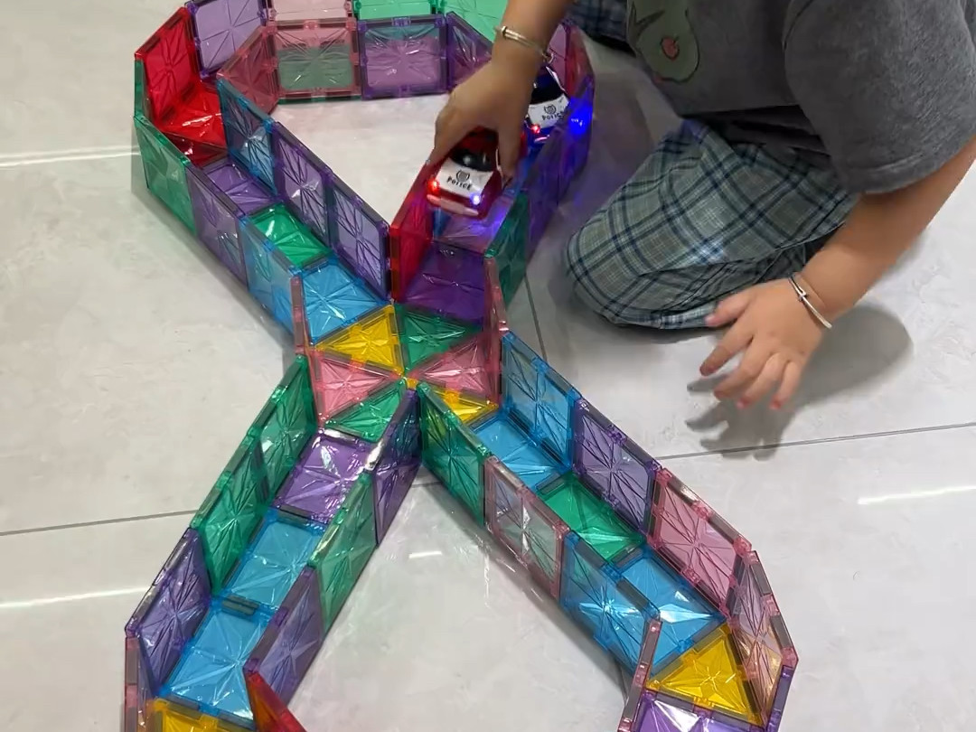 孩子用磁力片围出长轨道，发光小车在里面跑